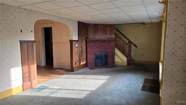 living room with wallpapered walls, arched walkways, a drop ceiling, stairs, and a brick fireplace