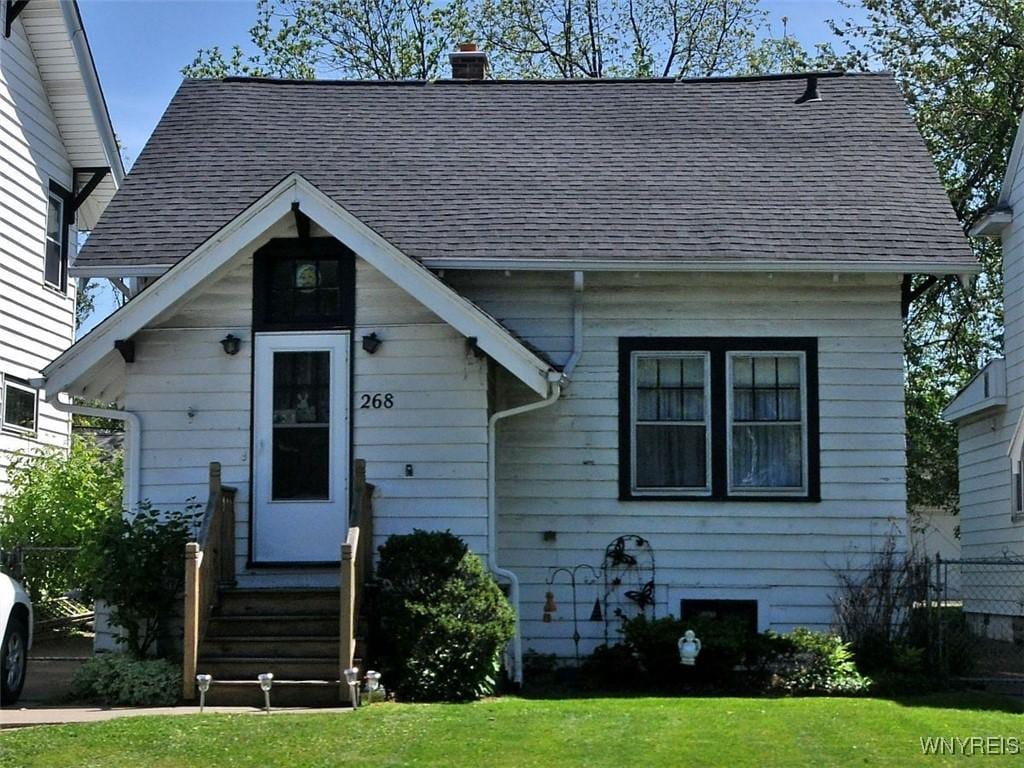 view of front of house featuring a chimney, entry steps, a front yard, and roof with shingles