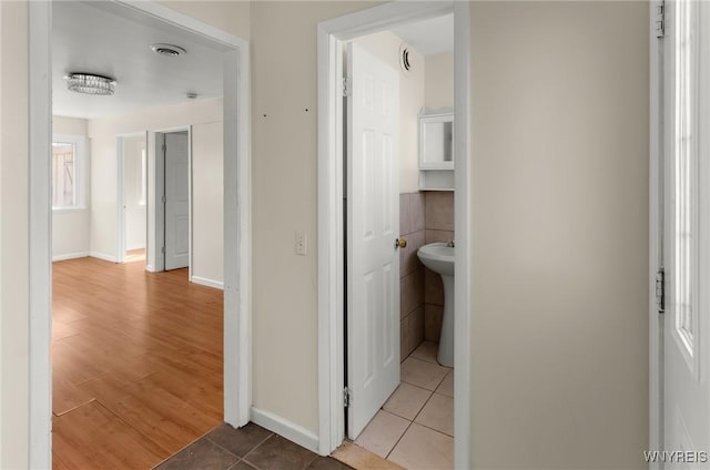 hall featuring light tile patterned floors, baseboards, and a sink