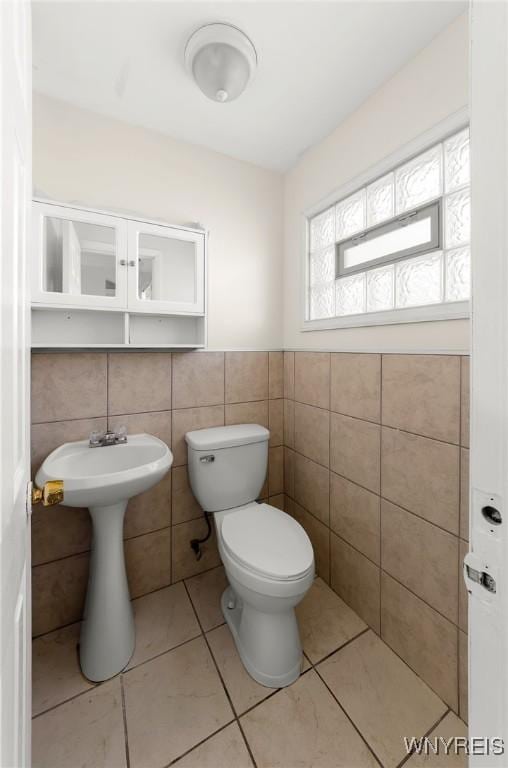 half bathroom featuring tile walls, toilet, tile patterned floors, and wainscoting