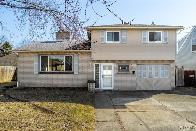 split level home with a patio, brick siding, a chimney, and fence