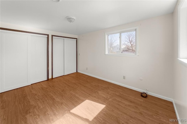 unfurnished bedroom with baseboards, multiple closets, and wood finished floors