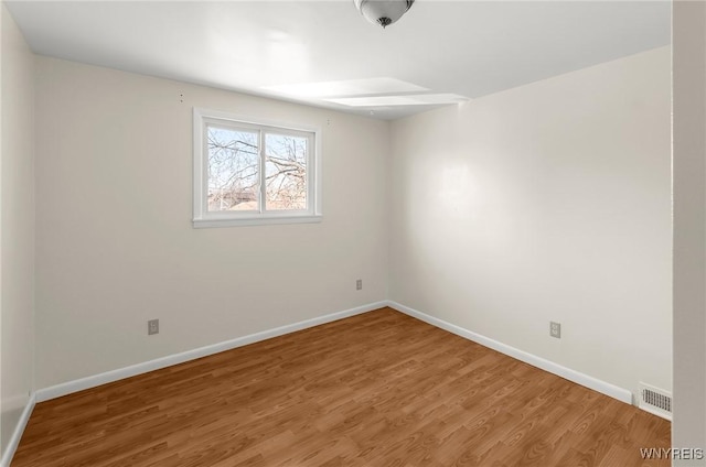 spare room with wood finished floors, visible vents, and baseboards