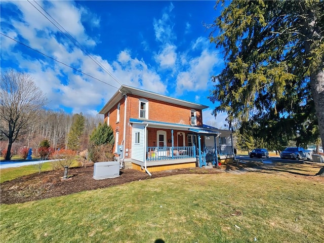 rear view of property featuring a yard, brick siding, and covered porch