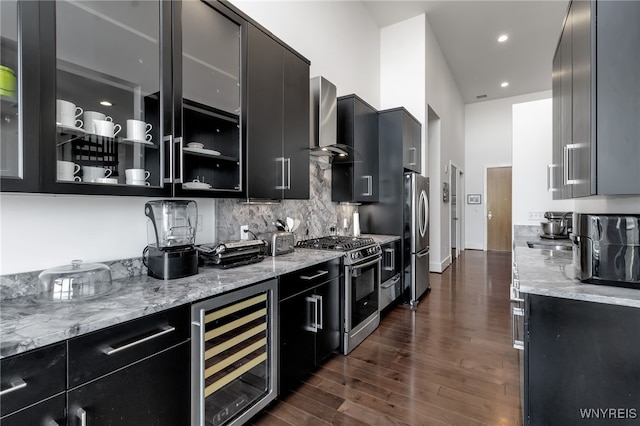 kitchen with wall chimney range hood, beverage cooler, dark cabinetry, and appliances with stainless steel finishes