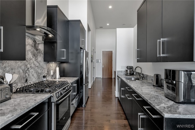 kitchen with wall chimney exhaust hood, a sink, dark cabinets, and stainless steel appliances