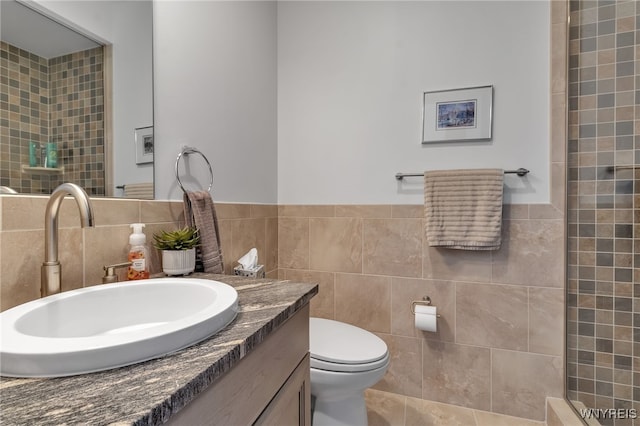 bathroom with toilet, tile walls, a tile shower, and vanity