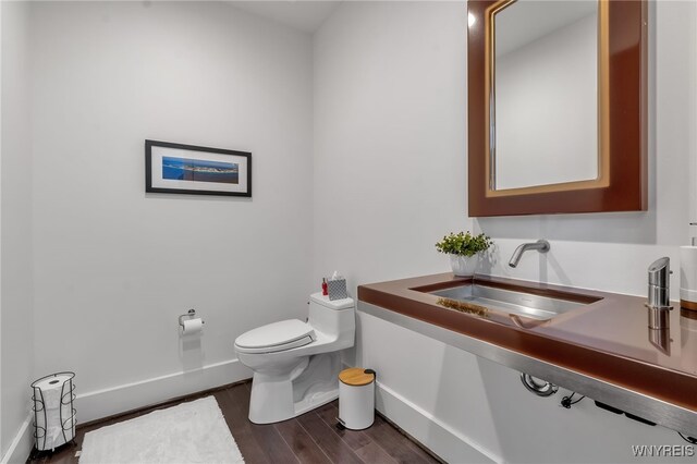half bath with toilet, wood finished floors, a sink, and baseboards