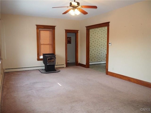 carpeted spare room with a baseboard heating unit, a wood stove, a ceiling fan, and baseboards