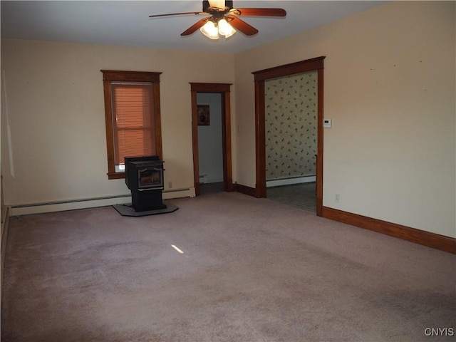 carpeted spare room featuring a baseboard heating unit, baseboards, ceiling fan, and a wood stove