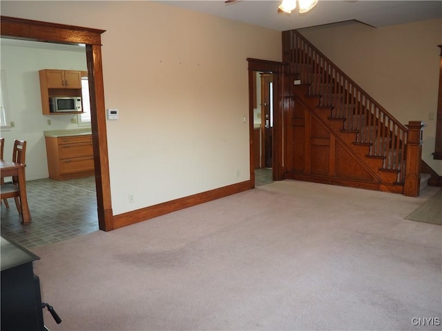 living room featuring stairway, light carpet, baseboards, and ceiling fan