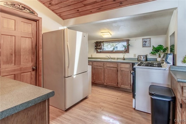 kitchen with a sink, freestanding refrigerator, range with gas cooktop, light wood finished floors, and wood ceiling