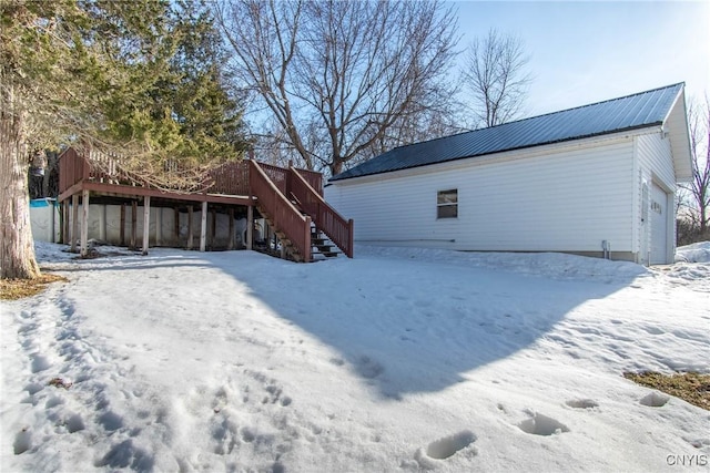 snow covered house with metal roof, an outbuilding, a wooden deck, and stairway