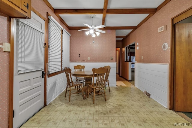 dining area with beam ceiling, a ceiling fan, wainscoting, and wallpapered walls