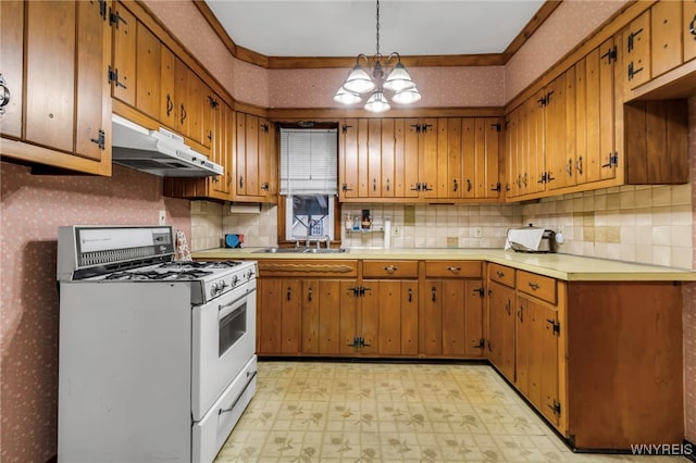 kitchen featuring brown cabinetry, light floors, wallpapered walls, gas range gas stove, and under cabinet range hood