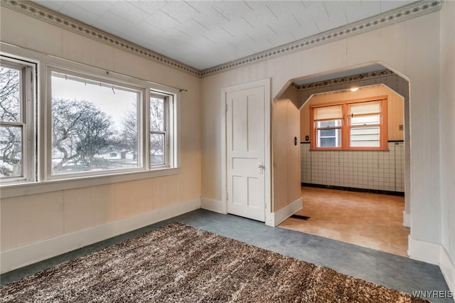 unfurnished room with arched walkways, a healthy amount of sunlight, and baseboards