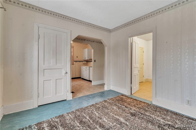 carpeted spare room featuring baseboards, arched walkways, and wallpapered walls