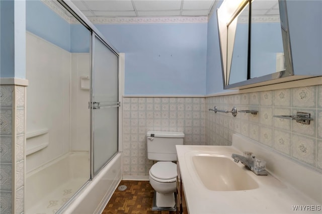 bathroom with bath / shower combo with glass door, toilet, wainscoting, vanity, and a paneled ceiling