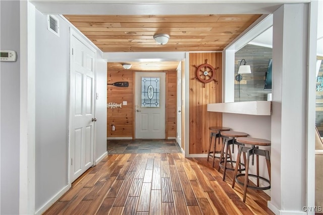 foyer entrance with wood ceiling, wood finished floors, visible vents, and wood walls