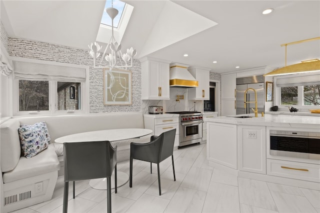 kitchen with premium range hood, a notable chandelier, decorative light fixtures, premium appliances, and white cabinetry