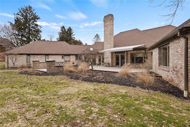 rear view of property featuring a patio, a yard, and a chimney