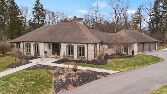 french country inspired facade with brick siding, a front lawn, a chimney, driveway, and an attached garage