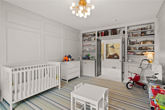 bedroom featuring a crib, ornamental molding, light carpet, an inviting chandelier, and a decorative wall