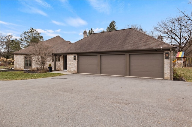 view of front of home featuring brick siding, an attached garage, roof with shingles, a chimney, and driveway