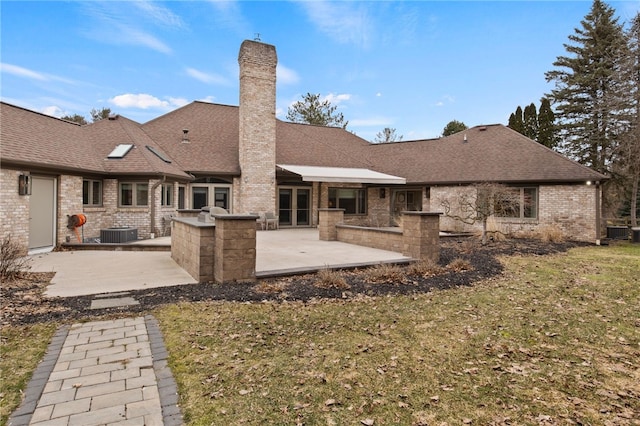 back of house featuring a shingled roof, central AC, a chimney, a yard, and a patio