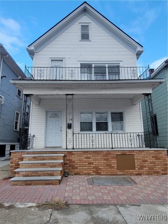 view of front of property featuring a porch, a balcony, and brick siding