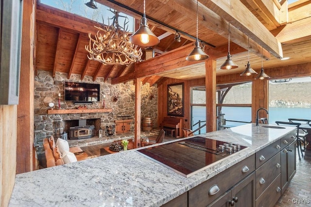 kitchen with beamed ceiling, a sink, light stone counters, black electric stovetop, and wood ceiling