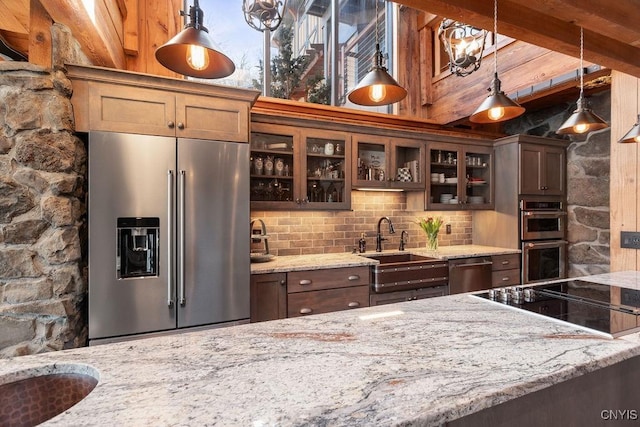 kitchen featuring glass insert cabinets, light stone countertops, decorative backsplash, stainless steel appliances, and a sink