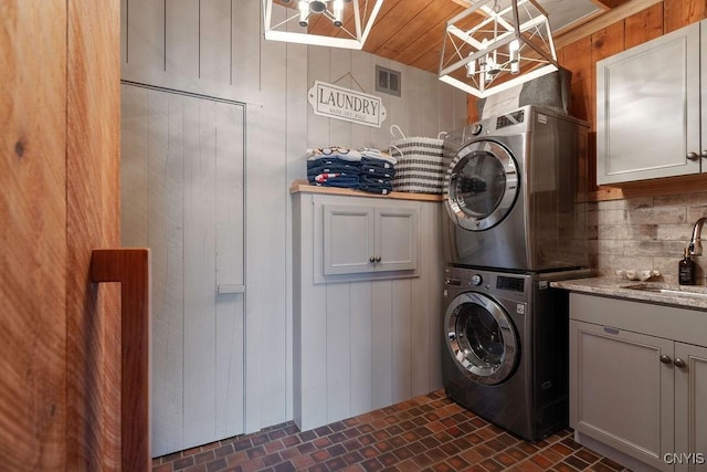 washroom featuring visible vents, cabinet space, brick floor, a sink, and stacked washer and dryer