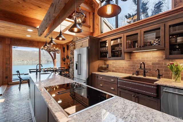 kitchen with a sink, appliances with stainless steel finishes, an inviting chandelier, brick floor, and decorative backsplash