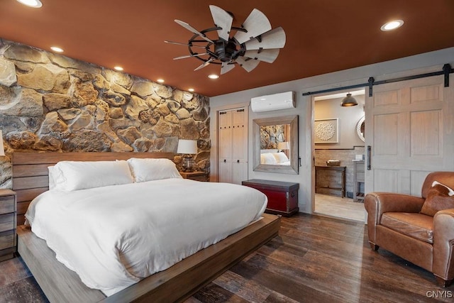 bedroom featuring wood finished floors, a wall mounted AC, ensuite bath, recessed lighting, and a barn door