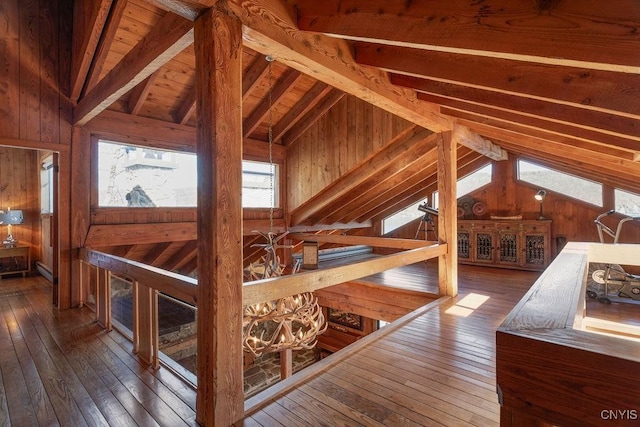 hallway featuring hardwood / wood-style floors, lofted ceiling with beams, wooden walls, and an upstairs landing