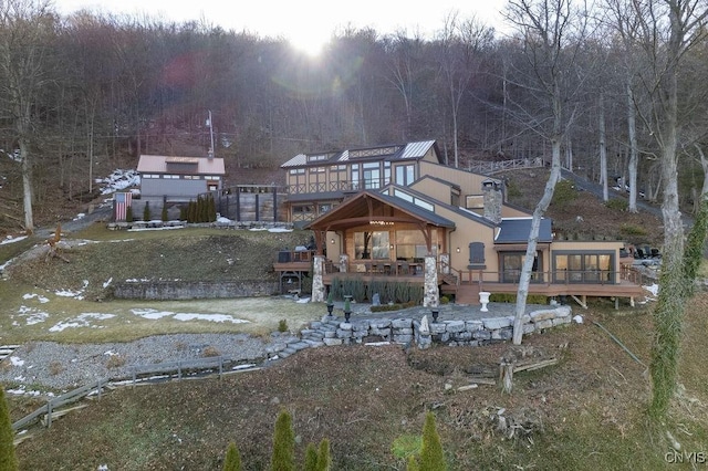 back of house with a deck, a chimney, and a wooded view