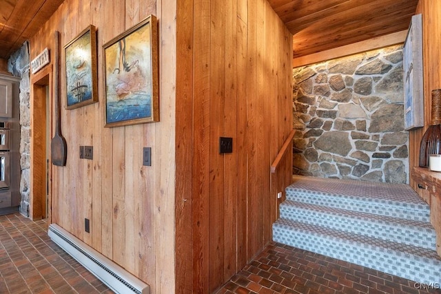 stairway featuring brick floor, a baseboard heating unit, wooden walls, and wooden ceiling