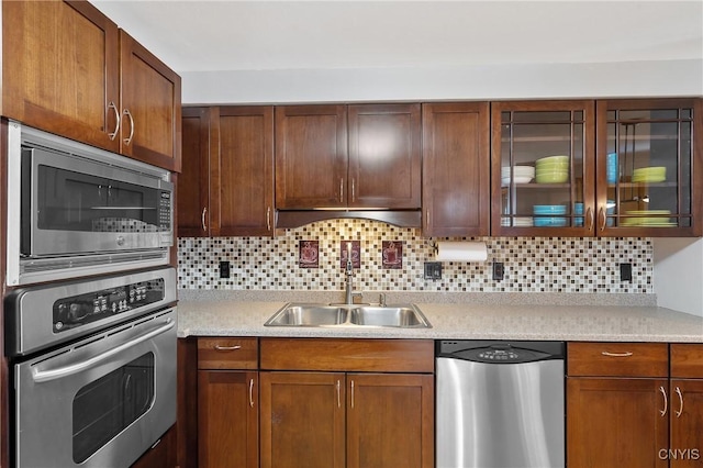 kitchen with a sink, stainless steel appliances, light countertops, glass insert cabinets, and backsplash