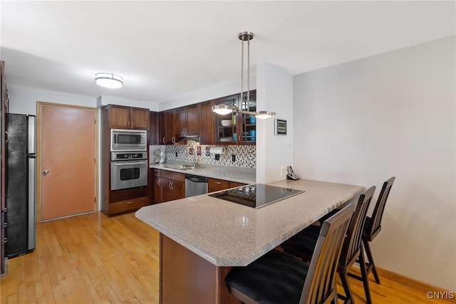 kitchen with a sink, light wood-style floors, appliances with stainless steel finishes, and a peninsula