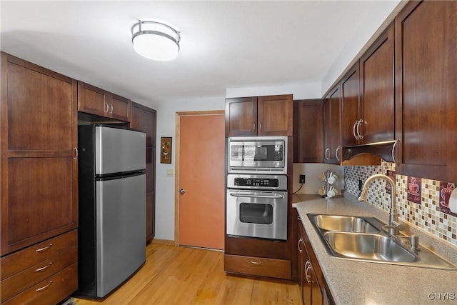 kitchen featuring light wood-style flooring, a sink, light countertops, appliances with stainless steel finishes, and tasteful backsplash