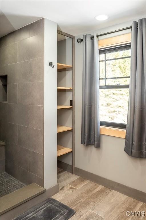 bathroom with baseboards, wood finished floors, and a tile shower