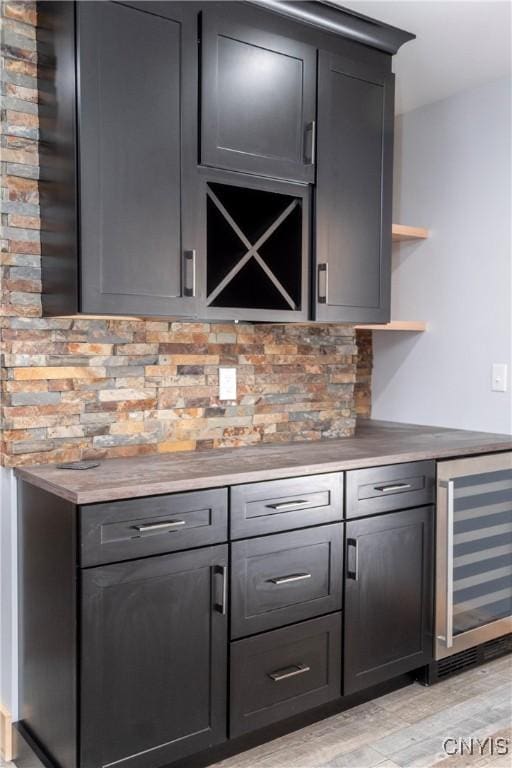 bar with a bar, wine cooler, light wood-style flooring, and tasteful backsplash