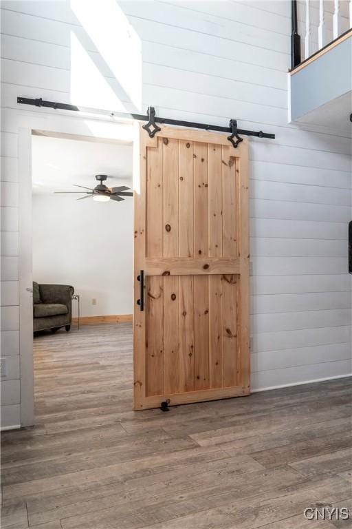 interior space with a barn door, wooden walls, a ceiling fan, and wood finished floors