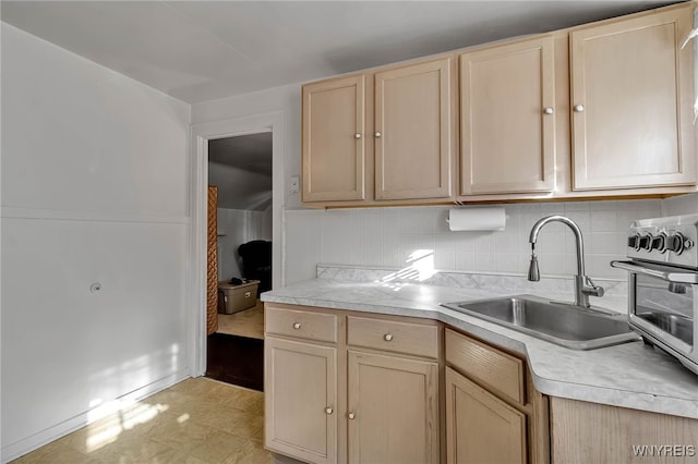 kitchen with light brown cabinetry, backsplash, light countertops, and a sink