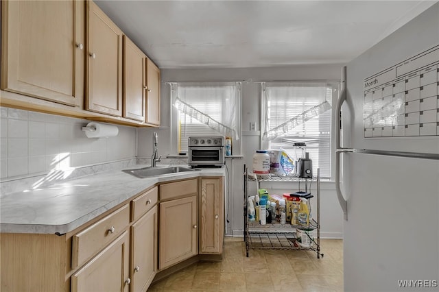 kitchen featuring light brown cabinets, light countertops, freestanding refrigerator, and a sink