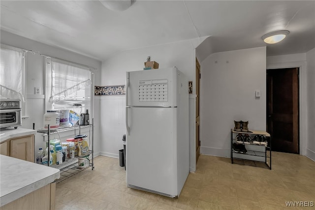 kitchen with a toaster, light floors, light countertops, vaulted ceiling, and freestanding refrigerator