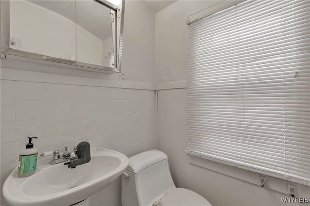 bathroom featuring tile walls, toilet, and a sink