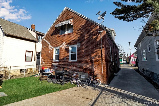 back of house with brick siding, a lawn, and fence