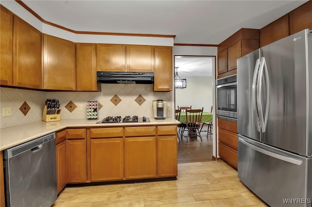 kitchen with under cabinet range hood, light countertops, decorative backsplash, light wood-style floors, and stainless steel appliances